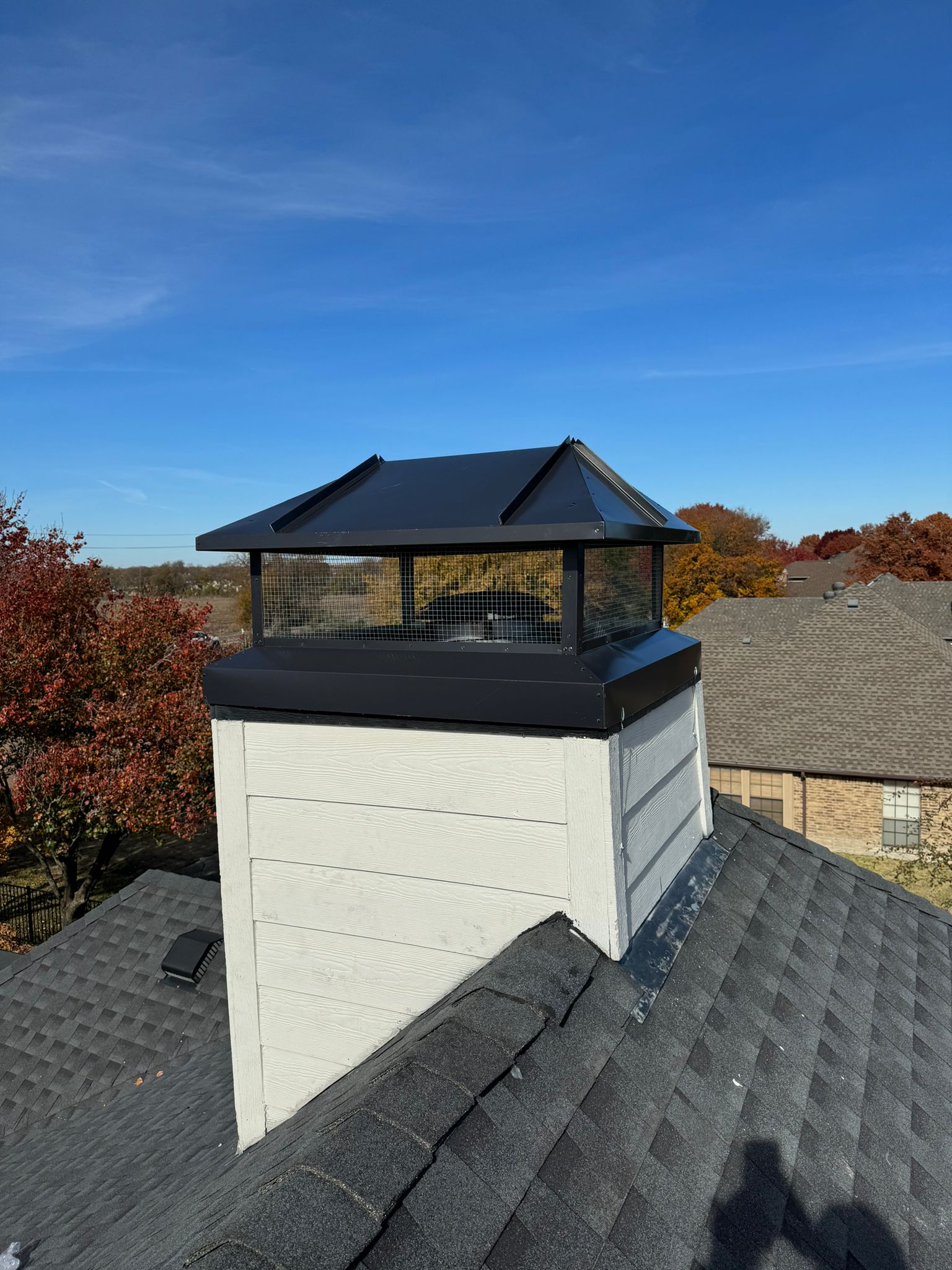 A roof top with a Chimney and trees in the horizon. A new Chimney Cap Installation in Dallas Texas for a Chimney Repair project.