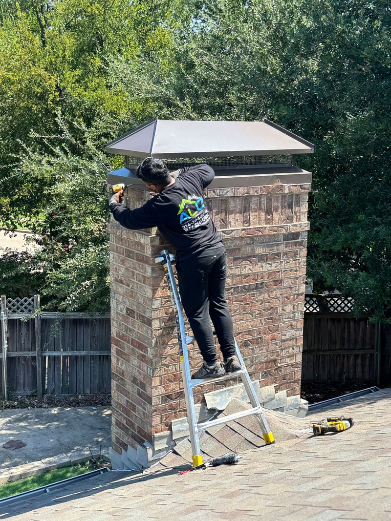 An ALC technician on a ladder fitting a new cap to a brick chimney