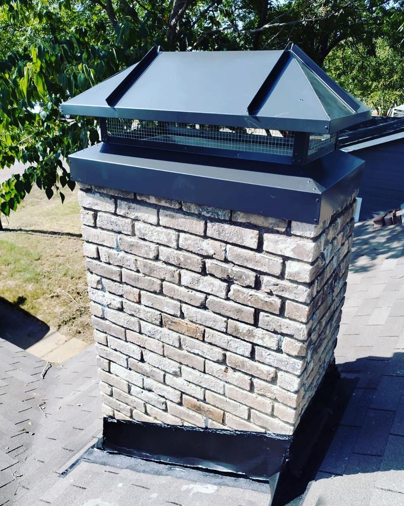 A new black stainless chimney cap installed on a white stone chimney against a clear sky