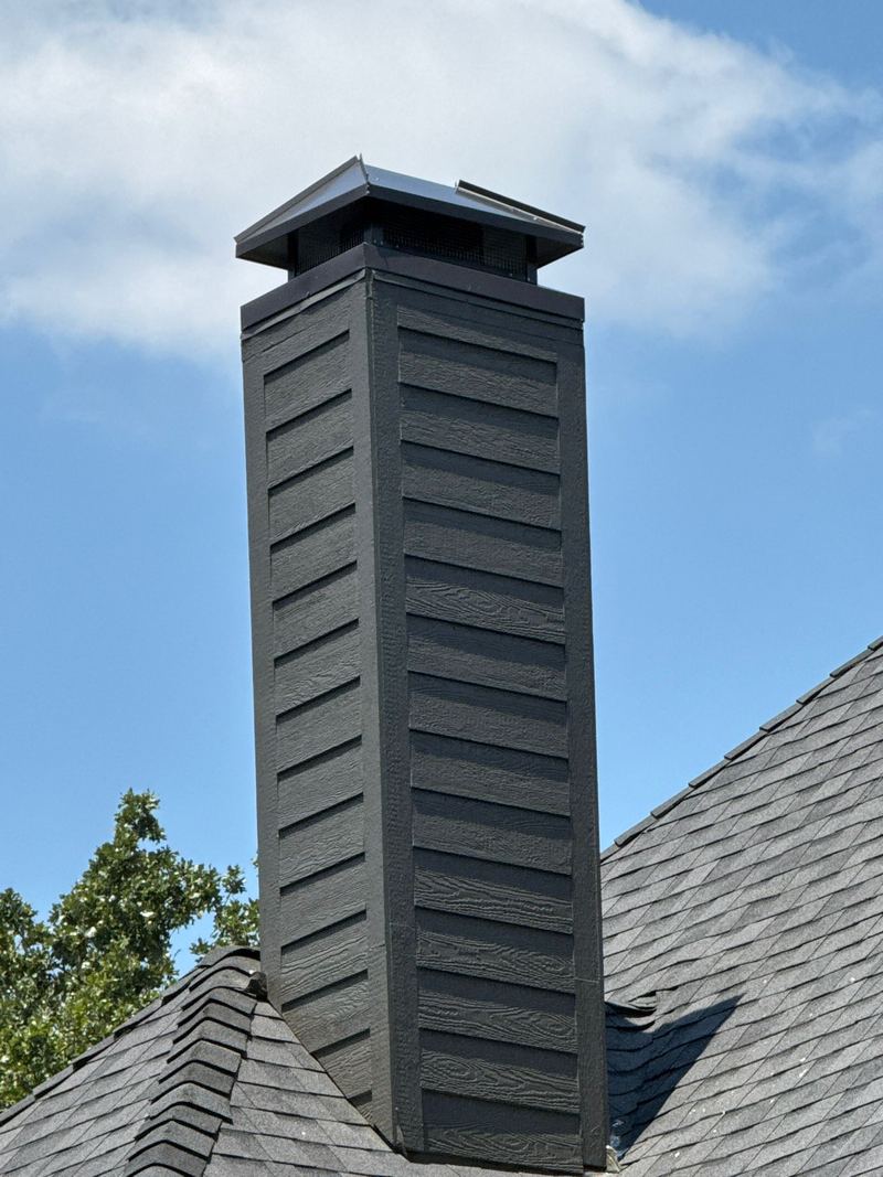 A dark metal chase cover and cap on a tall chimney chase above a shingle roof