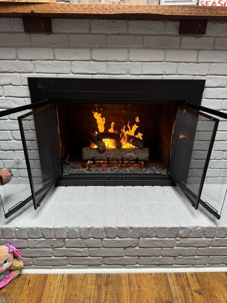 A clean fireplace with glass doors and a lit fire after servicing